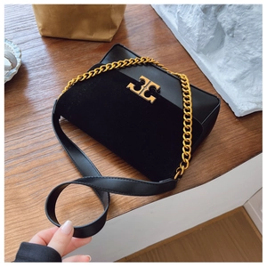 Detail of black crossbody bag with gold chain and metal logo on a wooden surface