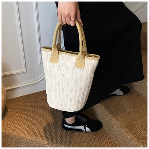 Detail of a woven straw tote bag with yellow handles shown in a casual lifestyle setting