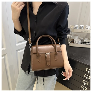 Model wearing dark brown leather crossbody bag with silver buckle and adjustable strap