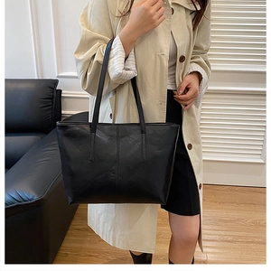 Detail view of a black leather tote bag featuring a vertical seam and long shoulder straps