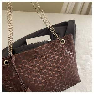 Detail of a brown tote bag with logo pattern, gold chain straps on a textured surface