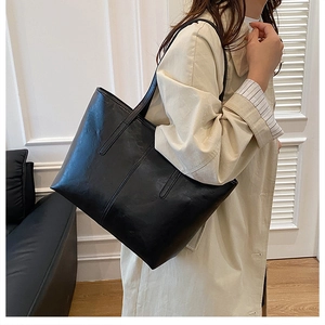 Side view of model carrying a large black PU leather tote bag in a minimalist room