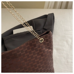 Close-up of dark brown tote bag featuring textured letter printing and gold chain strap