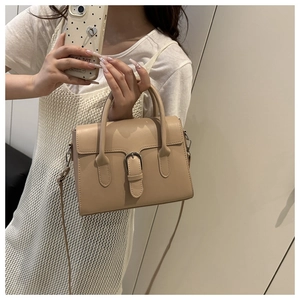 Detail of a beige handbag with a flap closure, buckle decor, and slim leather straps