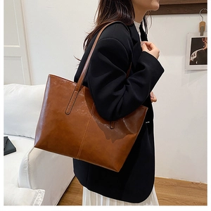 Detail view of large brown oil wax leather tote bag worn with a casual professional outfit