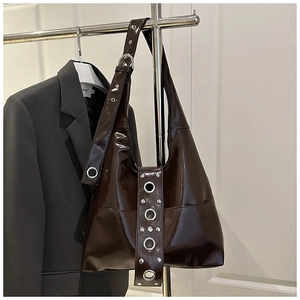 Detail of dark brown patent leather hobo bag with large silver metal grommets and rivets