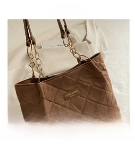Close-up of quilted dark brown suede tote bag with gold chain strap and brand plate