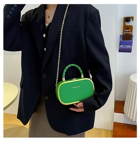 Green structured bag with gold frame, spiral handle and chain strap on a black suit