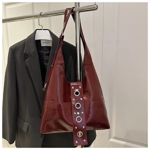 Macro detail of wine red patent leather shoulder bag with silver rivet and eyelet accents