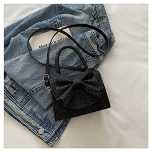 Détail du sac pailleté noir avec grand nœud et finitions dorées sur un jean bleu