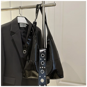 Detail of glossy black patent leather tote bag featuring stylish silver metal eyelets
