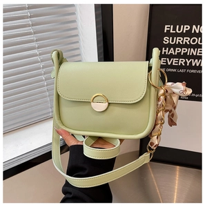 Detail of light green leather crossbody bag with gold buckle and polka dot scarf accessory