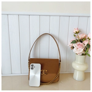 Brown leather crossbody bag with gold logo and chain next to a smartphone for scale