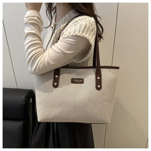 Detailed view of cream canvas tote bag with brown leather trim worn by a model