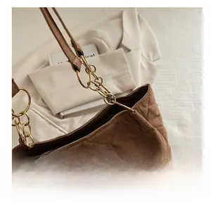 Detail of brown suede tote bag featuring quilted stitching and gold metal ring hardware