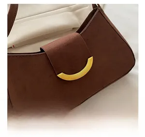 Close-up of dark brown suede baguette bag featuring a decorative crescent gold metal buckle