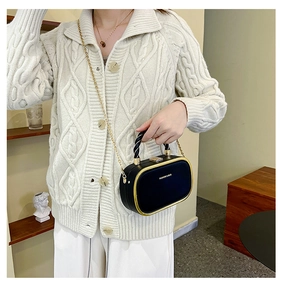 Detail of black box bag with gold metal trim and chain strap against a white outfit