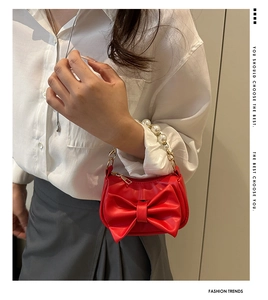 Close-up of red mini handbag featuring a large bow and elegant pearl handle