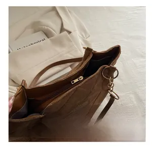 Detail view of smooth gold zipper and diamond quilted stitching on brown suede tote bag