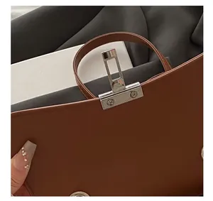 Detail showing the silver metal lock buckle and stitching on the brown leather handbag