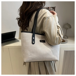 Close-up of canvas tote bag with black leather handles and branded logo patch detail