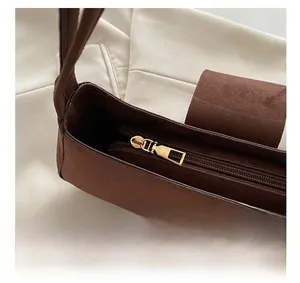 Close-up of brown suede baguette bag featuring smooth gold metal zipper and magnetic snap