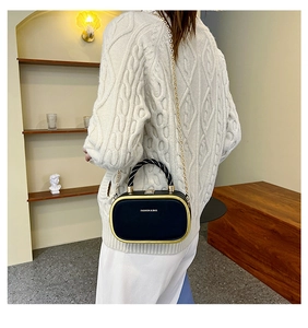 Detail of a black structured box bag with gold metal trim and woven spiral handle
