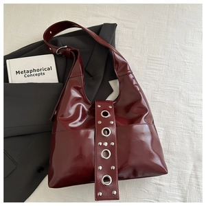 Détail du sac bandoulière en cuir brillant bordeaux avec rivets et œillets métalliques