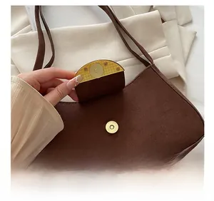 Detailed close-up of golden round magnetic buckle on dark brown suede baguette bag