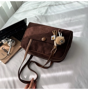 Detail of brown suede tote bag with plush charm and flap closure on a soft bed