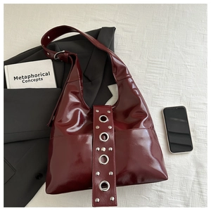 Close-up of deep burgundy glossy leather hobo bag featuring stylish silver metal eyelets