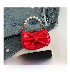 Detail of red bow handbag with pearl handle shown next to a smartphone for scale