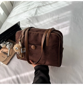Detail view of brown suede tote bag with plush charm and handle on a bed in natural sunlight