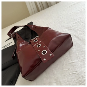 Detail of burgundy patent leather hobo bag featuring decorative silver metal eyelets