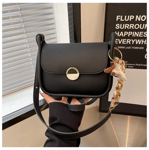 Close-up of black matte crossbody bag with round metal buckle and floral silk scarf detail
