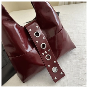Close-up of glossy deep red leather handbag with silver metallic eyelets and rivets