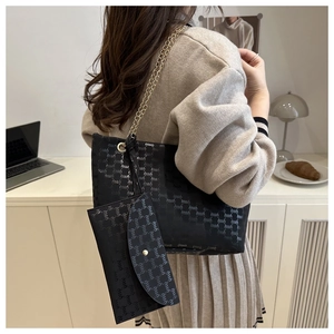 Detail of black tote bag set with gold chain strap on model in neutral interior