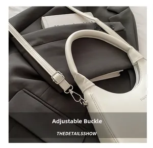 Detail view of the adjustable silver buckle and thin shoulder strap on a white crescent bag