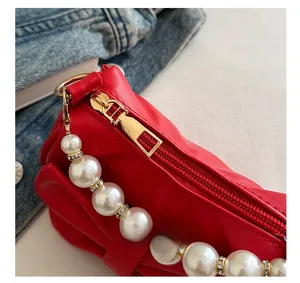 Detail of red faux leather clutch featuring gold zipper and pearl rhinestone chain strap