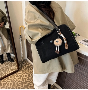 Close-up of black suede shoulder bag with plush charm and long strap detail