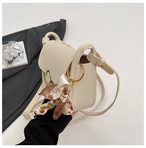 Detail of cream crossbody bag with large gold ring and brown polka dot silk bow decoration
