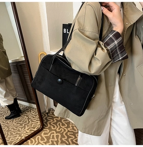 Detail of black suede shoulder bag with button decor and fine stitching on trench coat