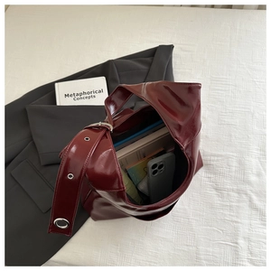 Detail of dark red patent leather tote bag with wide strap and metallic grommets