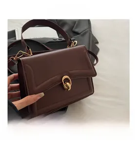 Detailed close-up of dark brown leather handbag featuring a gold twist clasp and metal strap hook