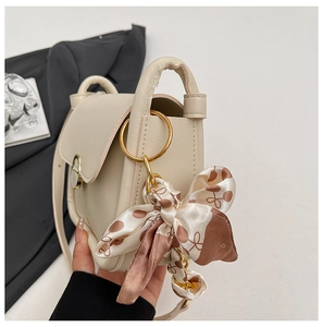 Detail of beige mini crossbody bag featuring a gold ring and decorative silk scarf