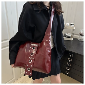 Close-up of burgundy patent leather tote with metal rivets and eyelet strap details