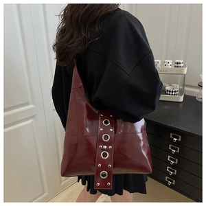 Detail of dark red high-gloss shoulder bag featuring vintage silver stud accents and eyelets