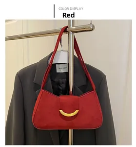 Detailed view of a red suede underarm bag with gold crescent buckle on a metal stand