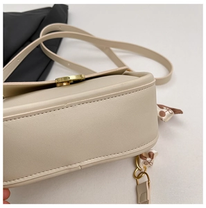 Detail view of beige crossbody bag with gold buckle, fine stitching and silk scarf accessory