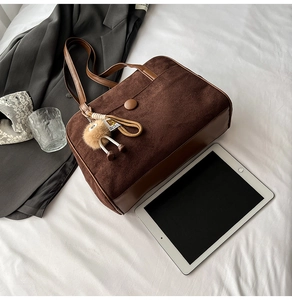 Macro shot of dark brown suede shoulder bag with leather trim and plush pendant